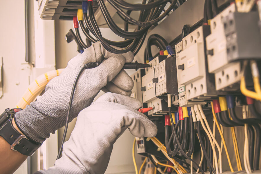 Electricity and electrical maintenance service, Engineer hand holding AC voltmeter checking electric current voltage at circuit breaker terminal and cable wiring main power distribution board.